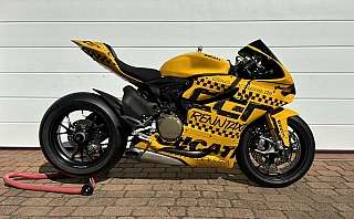 Ein gelbes Ducati Motorrad mit auffälligen Aufklebern auf einem Pflastersteinboden.