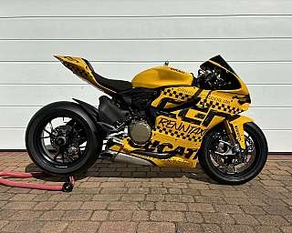 Eine gelbe Ducati Rennmaschine mit auffälligen Aufklebern auf einem Parkplatz.
