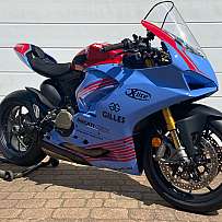 Ein blaues Ducati Rennmotorrad auf einem Ständer vor einer weißen Wand.