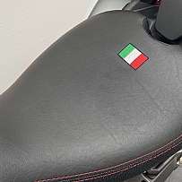 Nahaufnahme eines Motorradsitzes mit roter Naht und italienischer Flagge.