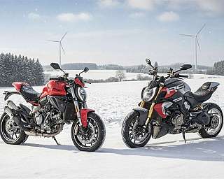 Zwei Ducatis stehen in einer verschneiten Landschaft mit Windrädern.