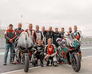 Eine Gruppe von Motorradfahrern posiert mit ihren Motorrädern auf der Rennstrecke.
