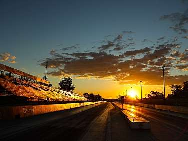 Eine Dragstrip mit leeren Tribünen und Sonnenuntergang im Hintergrund.