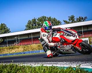 Ein Motorradfahrer in voller Fahrt auf einer Rennstrecke mit Tribünen im Hintergrund.