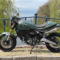 Ein grünes Motorrad steht an einer Brücke mit Bäumen im Hintergrund.