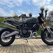 Ein grünes Ducati Motorrad steht an einem Flussufer mit Bäumen im Hintergrund.