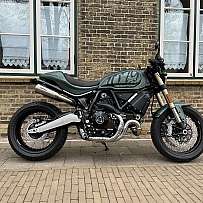 Ein grünes Ducati Motorrad steht vor einer Backsteinmauer mit Fenstern.