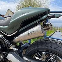 Detailaufnahme eines Motorrads mit SC-Project-Auspuff und Kanal im Hintergrund.
