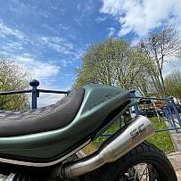 Detailaufnahme eines Motorradsitzes und Auspuffs vor blauem Himmel.