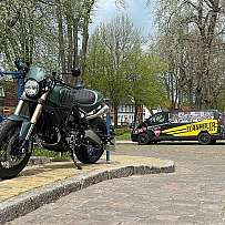 Ein grünes Motorrad steht auf einem gepflasterten Weg neben einem Lieferwagen.