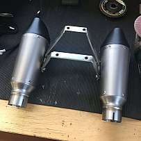 Zwei Motorrad-Auspuffanlagen mit Halterung auf einem Tisch.