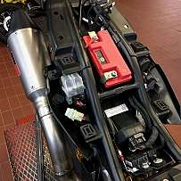 Detailansicht des Motorrads mit Batterie und Auspuffanlage.