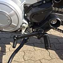 Detailaufnahme eines Motorrad-Antriebssystems mit Kette und Fußrasten.
