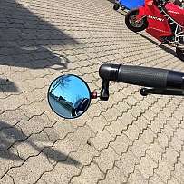Nahaufnahme eines Motorradspiegels mit reflektierter Landschaft.
