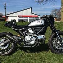 Ein Ducati Scrambler Motorrad auf einer grünen Wiese.
