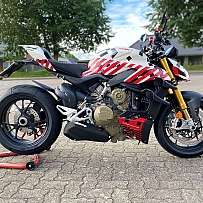 Ein sportliches Ducati Motorrad auf einem Parkplatz mit Bäumen im Hintergrund.