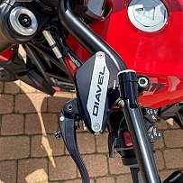 Nahaufnahme eines Motorradlenkers mit verschiedenen Bedienelementen und einem roten Tank.