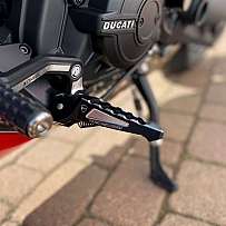 Detailaufnahme der Fußrasten eines Ducati Motorrads auf einem Pflastersteinboden.