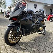 Ein schwarzes Sportmotorrad mit goldenen Felgen vor einem Motorradgeschäft.