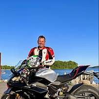 Ein Motorradfahrer posiert stolz neben seiner Ducati Panigale am Wasser.