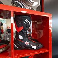 Schwarze und rote Ducati Motorradstiefel auf einem Regal.