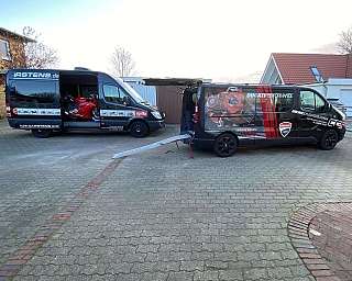 Zwei Transporter mit Motorrädern in einem Hof, einer mit Ducati und einer mit Aprilia.