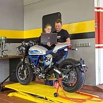Zwei Personen arbeiten an einem Motorrad in einer Werkstatt.