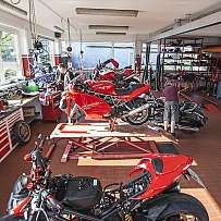 Eine Motorradwerkstatt mit mehreren Ducati-Motorrädern und Mechanikern bei der Arbeit.