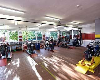 Eine Motorradwerkstatt mit mehreren Motorrädern und Mechanikern bei der Arbeit.