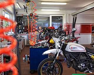 Eine Motorradwerkstatt mit mehreren Motorrädern und Werkzeugen im Hintergrund.